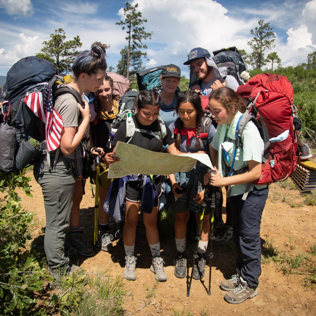 Members of crew 611-K front row: Isabelle DuPont- Moore, Sophia White (hidden), Grace Maready, Anita Richards, Ethan Boud, front row: Carolina Garcia, Elizabeth Nango and Jadyn Blake look at a map in front of Mount Baldy at Philmont Scout Ranch in Cimarron, New Mexico on Saturday, June 15, 2019.